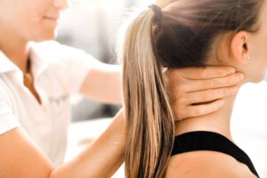 A pregnant person sitting on a couch with a support pillow, stretching gently with hands on lower back.