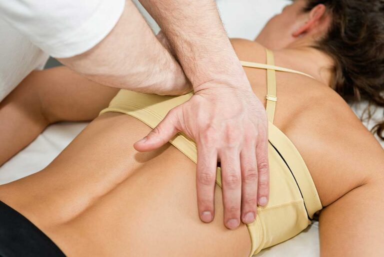 An older adult receives a gentle spinal adjustment from a practitioner in a bright, home-like clinic setting.