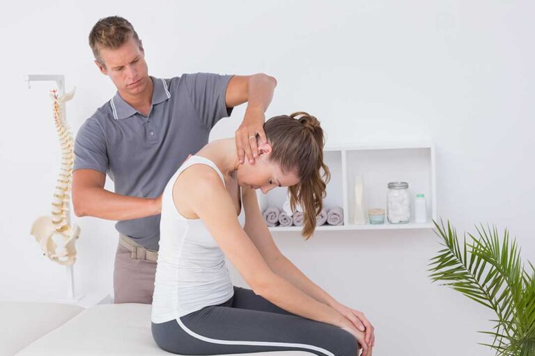 Patient in comfortable clothing discusses back pain and medical notes with a chiropractor in an examination room.